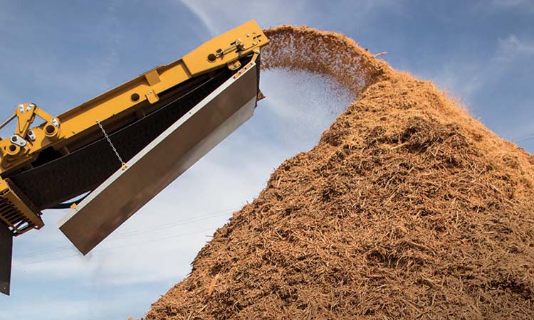 A Vermeer horizontal grinder releases wood waste product from a conveyor into a pile